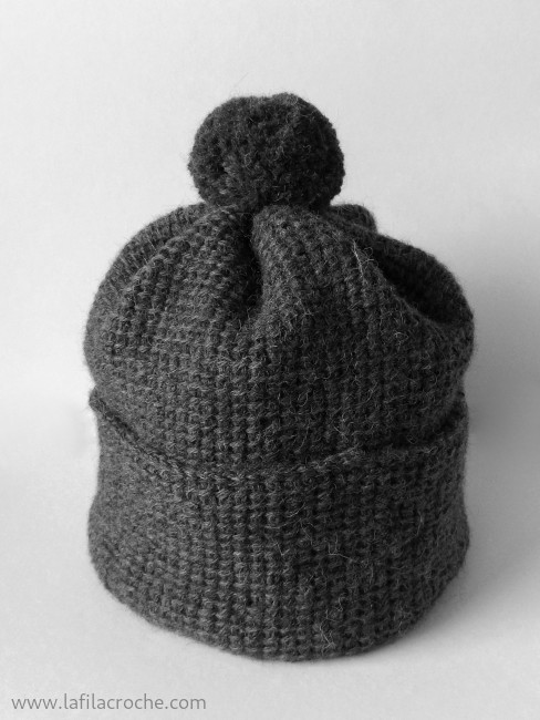 Bonnet en grosse laine grise fait au crochet tunisien, avec un pompon