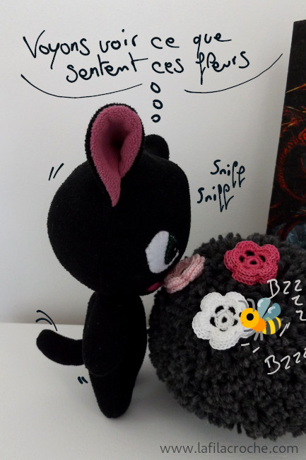 Chat en peluche qui sent des fleurs au crochet posées sur un pompon