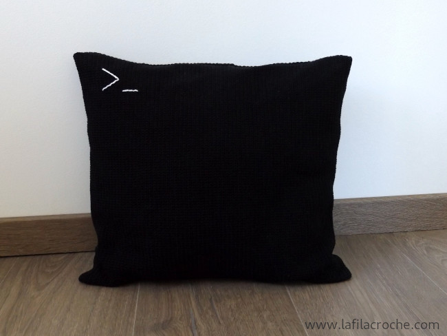 Housse de coussin noire au crochet avec les caractères >_ brodés en blanc en haut à gauche