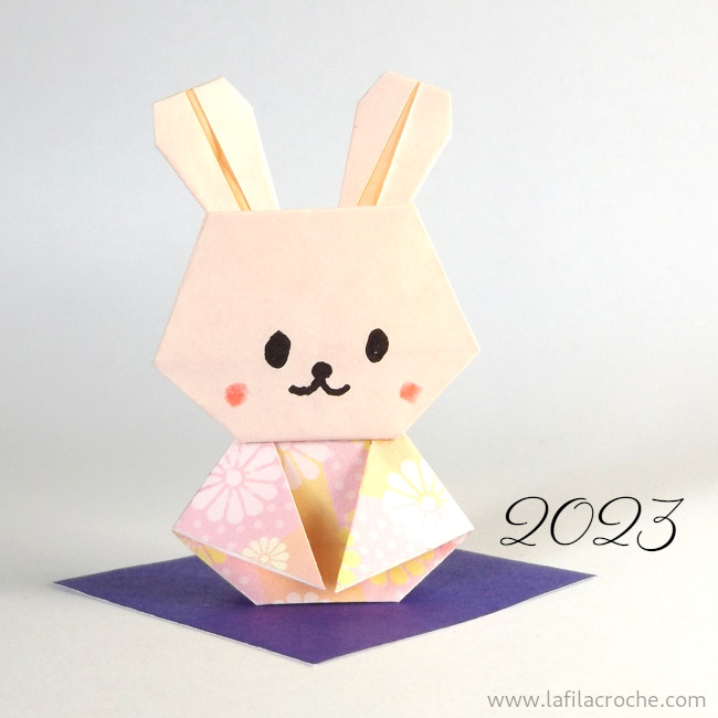 Lapin en origami posé sur un carré de papier violet, fond blanc et « 20203 » inscrit à côté.