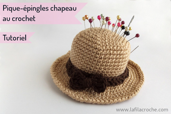 Un pique-épingles de couture en forme de chapeau, réalisé au crochet. Des épingles sont piquées dedans.