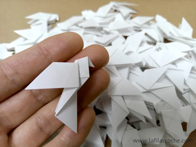 Une petite colombe origami posée dans ma main avec les 99 autres en dessous
