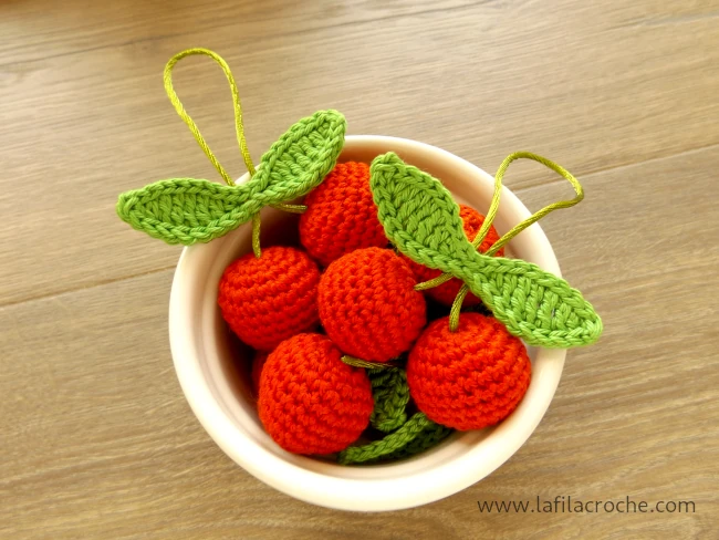 Des amigurumi cerises au crochet disposées dans un petit ramequin blanc en porcelaine