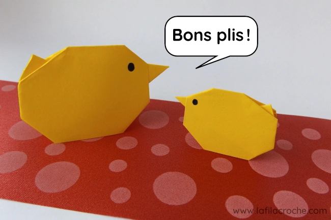 Deux poussins de printemps en origami posés sur un ruban rouge à pois avec, au-dessus, une bulle où il est écrit « Bons plis ! »